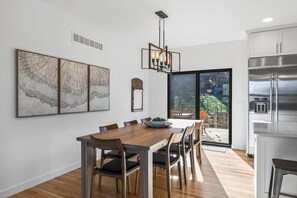A modern kitchen with a stainless steel refrigerator, a wooden dining table with chairs, and a large window overlooking a garden. - Modern 4 Bedrooms with 4 Ensuite Bathrooms - Perfect for Families & Groups (Riverside)