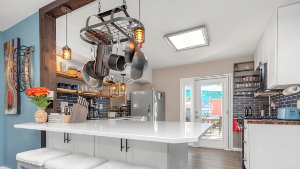 A modern kitchen with white cabinetry, a central island with bar stools, hanging pots, and a unique ceiling light fixture. - Modern 3-BedRoom House
Large Deck, Firepit, Chef's kitchen, King Suite (Clearwater)