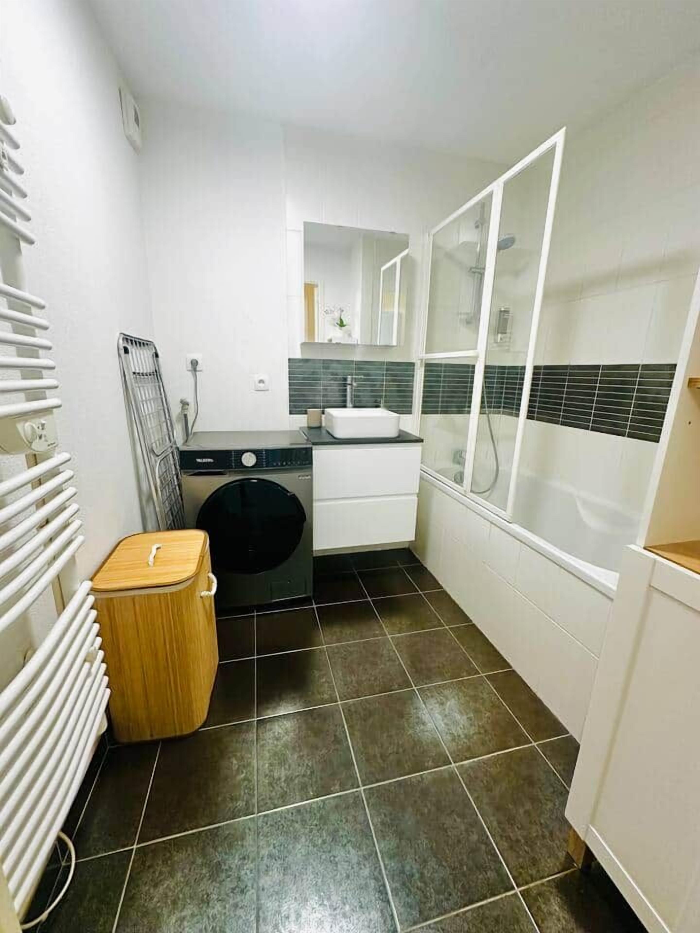Een kleine badkamer met een wasmachine, een wastafel, een spiegel en een douchecabine.