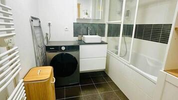 Een kleine badkamer met een wasmachine, een wastafel, een spiegel en een douchecabine.