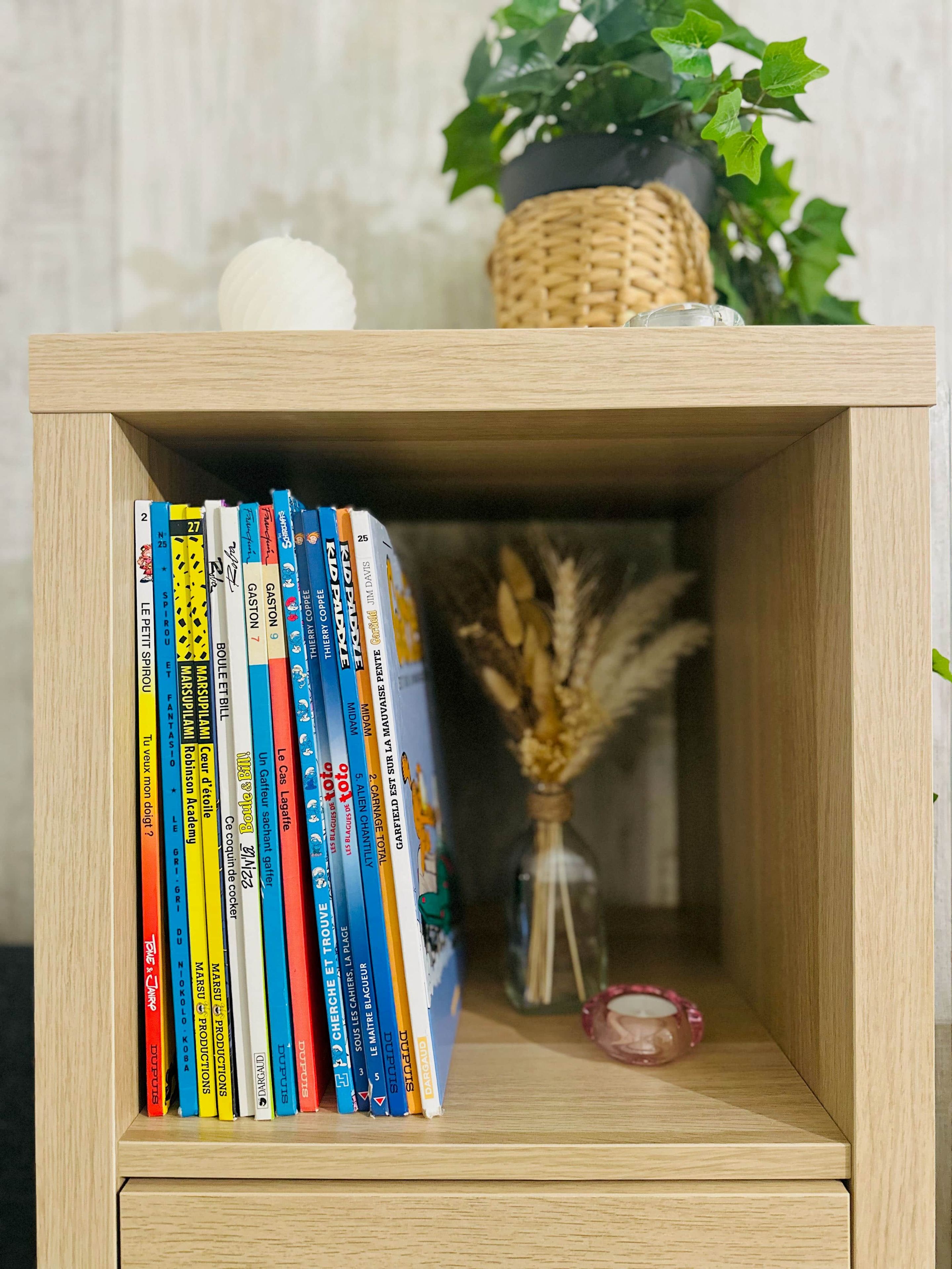 A wooden bookshelf with a variety of books and a small vase with dried plants.