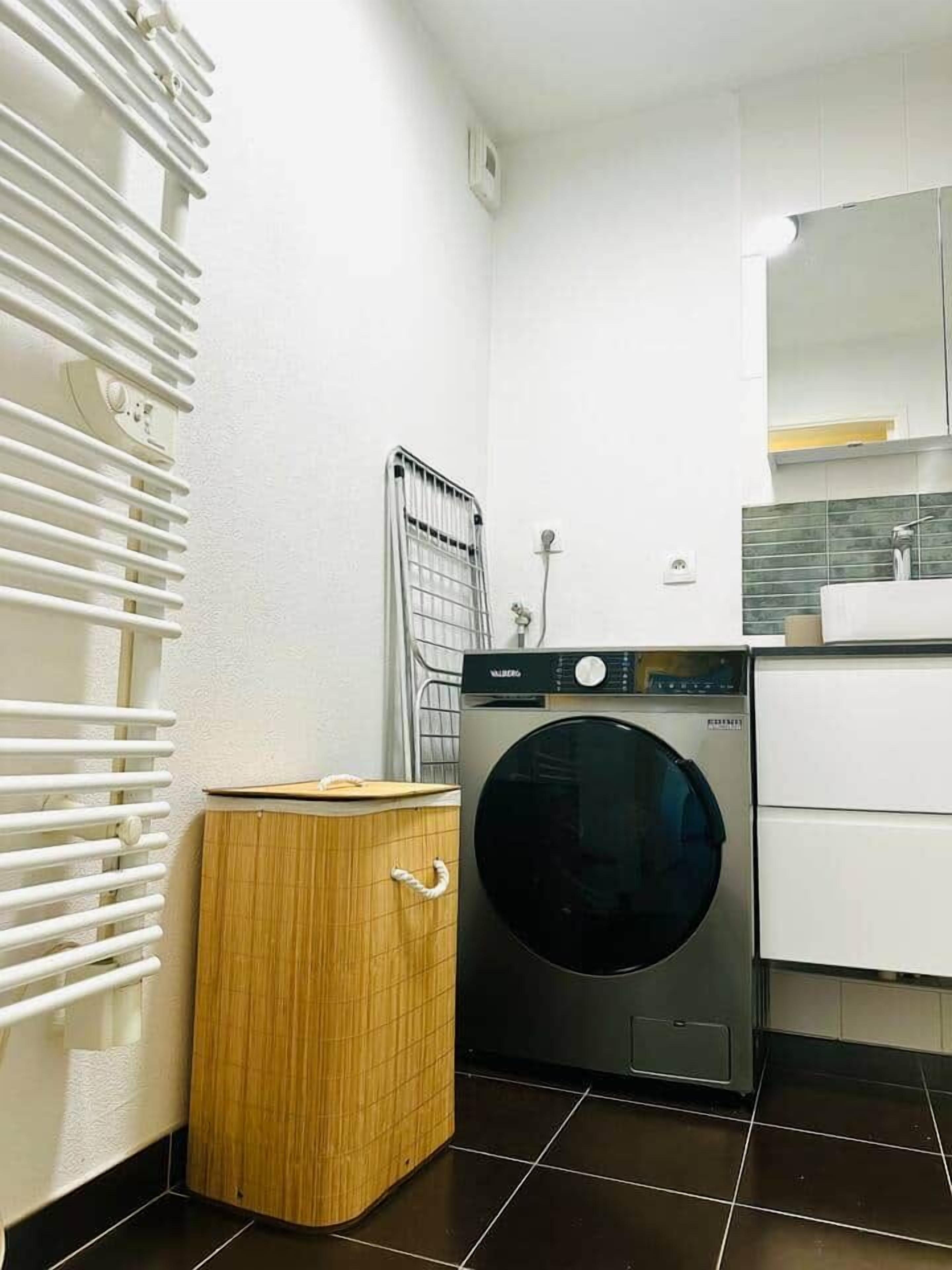A compact laundry room with a front-loading washing machine, a drying rack, and a small wooden cabinet.
