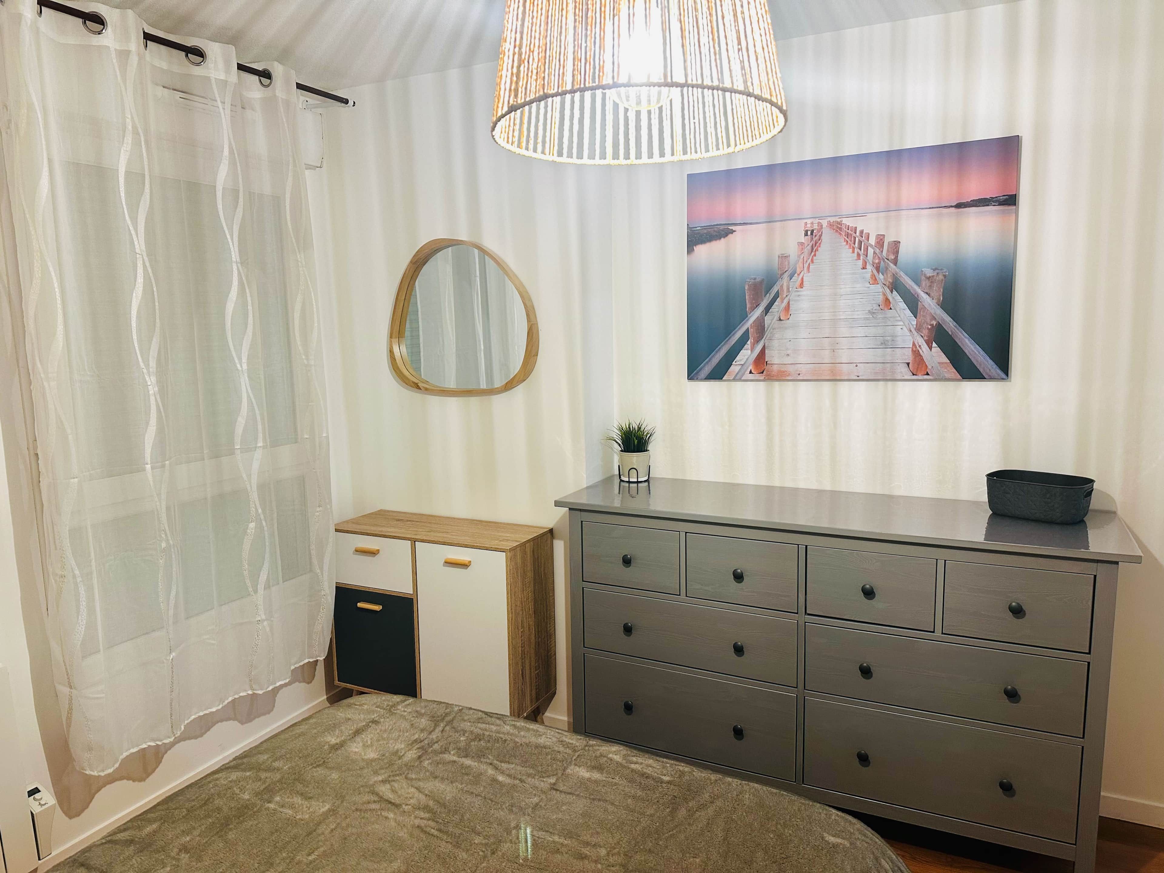 Et soveværelse med seng, kommode, spejl, et billede og en hængende lampe.