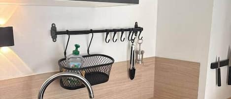 A kitchen with a black sink, wooden countertop, and a metal rack holding kitchen utensils.
