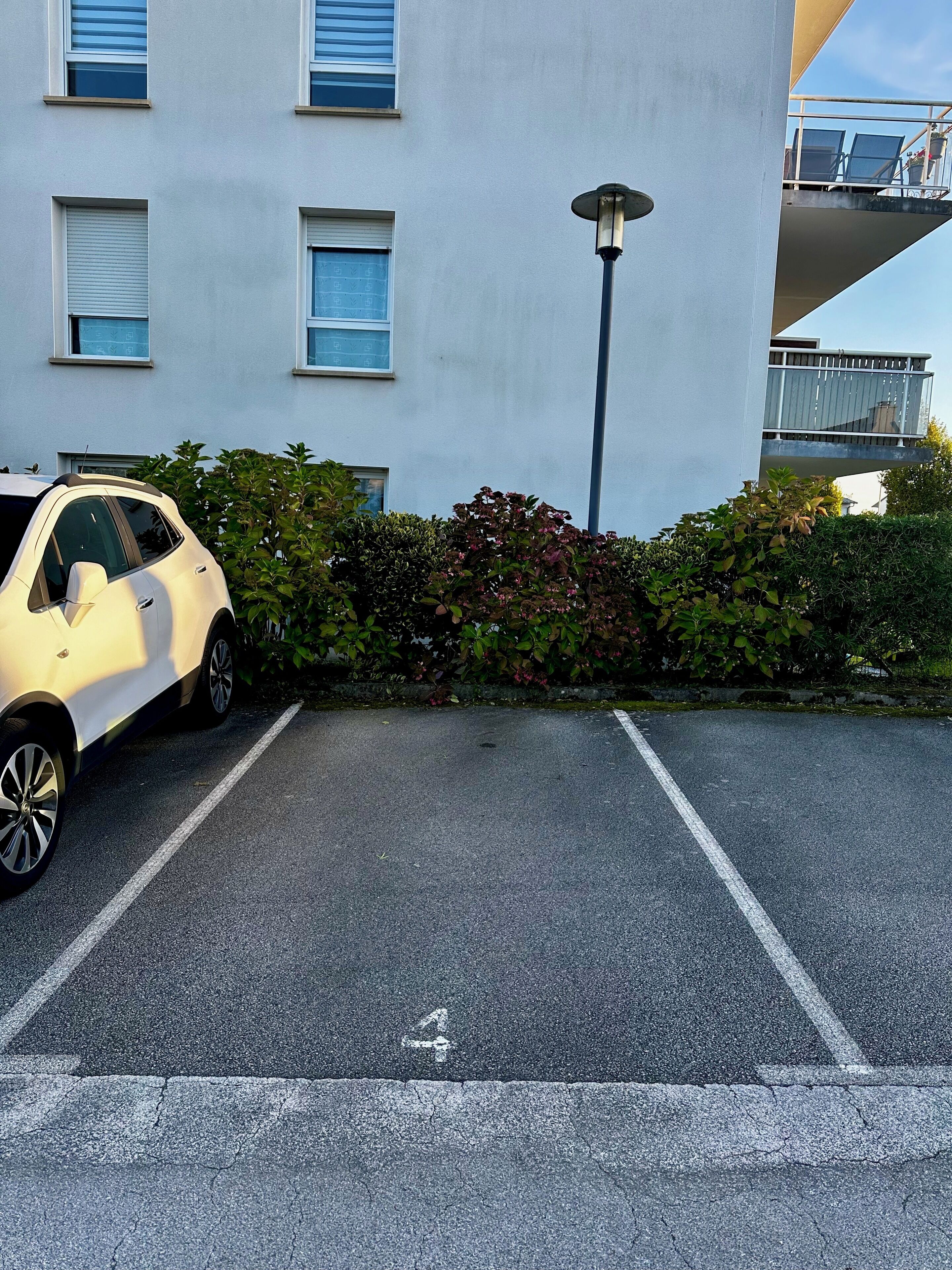 Un parking avec une voiture blanche, un lampadaire et un immeuble doté de nombreuses fenêtres et de balcons.