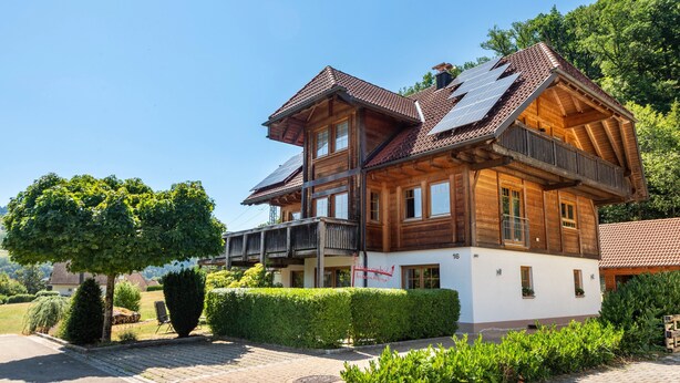 Een houten huis met twee verdiepingen, een balkon, zonnepanelen op het dak en een verzorgde tuin.
