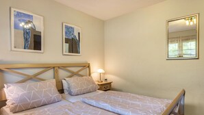 Een tweepersoonsbed met geometrische beddengoed, een nachtkastje met een lamp, en twee abstracte schilderijen aan de muur.