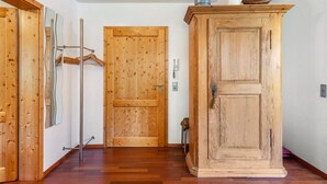 Een hal met houten vloer, een houten deur, een houten kast en een kapstok met hangers.