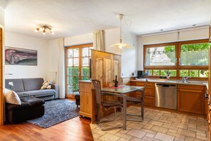 Un espace de vie compact comprenant un canapé, une table à manger, un coin cuisine et une grande fenêtre donnant sur un paysage verdoyant.