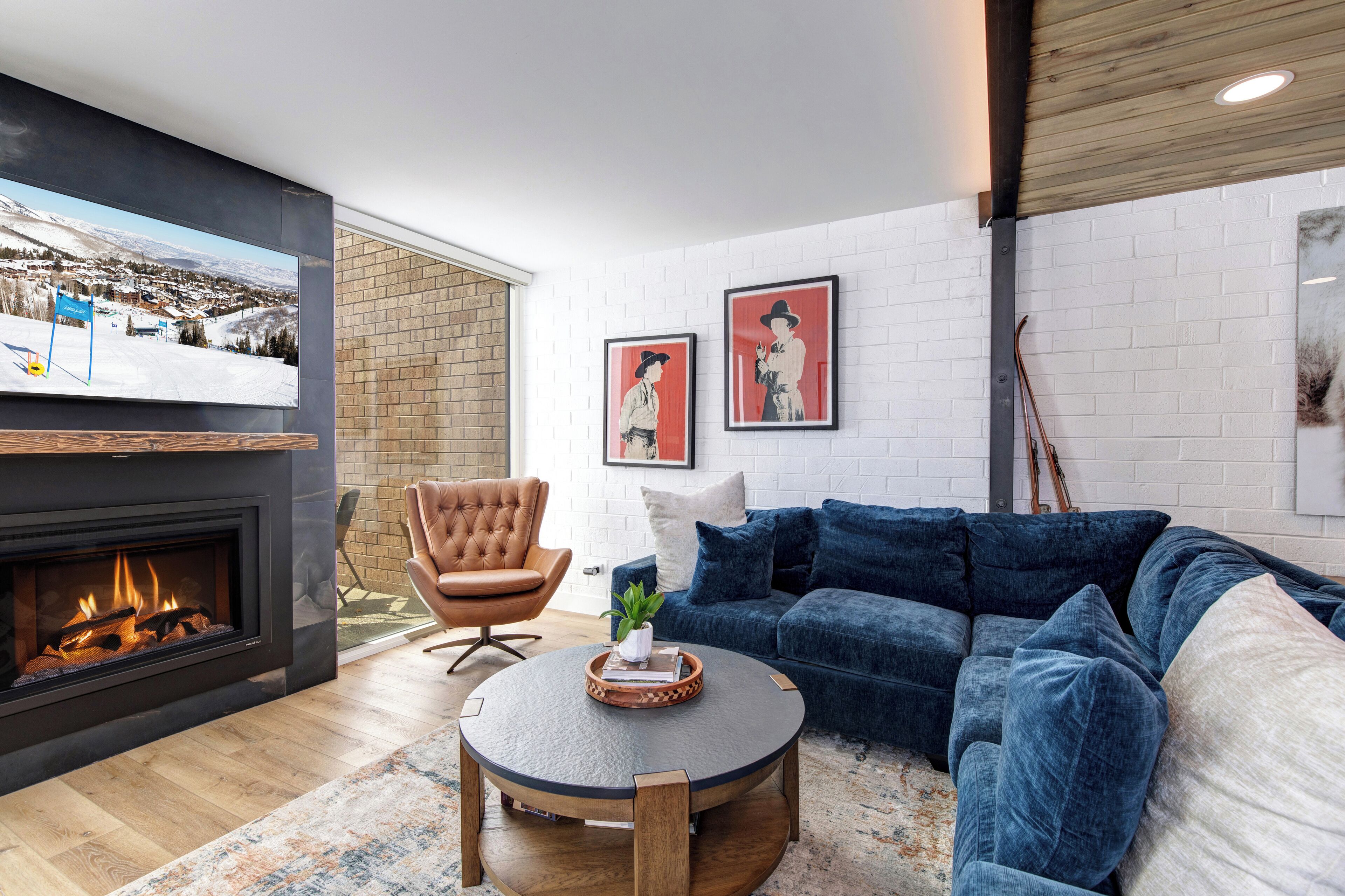 Una sala moderna con chimenea, un sofá azul, un sillón de cuero y un televisor de pantalla plana montado en la pared.