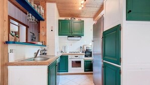 Eine kompakte Küche mit grünen Schränken, einer Holzarbeitsplatte, einem Spülbecken, einem Herd und einem Kühlschrank.