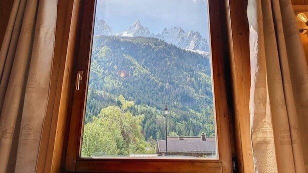 Ein Fenster mit Blick auf eine gebirgige Landschaft, Vorhänge und ein Holzrahmen.
