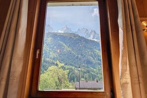 A window with a view of a mountainous landscape, curtains, and a wooden frame. - Chamonix Base Camp (Chamonix-Mont-Blanc)