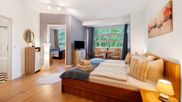 Une chambre d’hôtel moderne équipée d’un lit, d’une télévision, d’un bureau et offrant une vue sur la verdure.