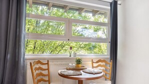 Un coin repas avec une table ronde, deux chaises en bois, une fenêtre avec des rideaux et un radiateur en dessous.