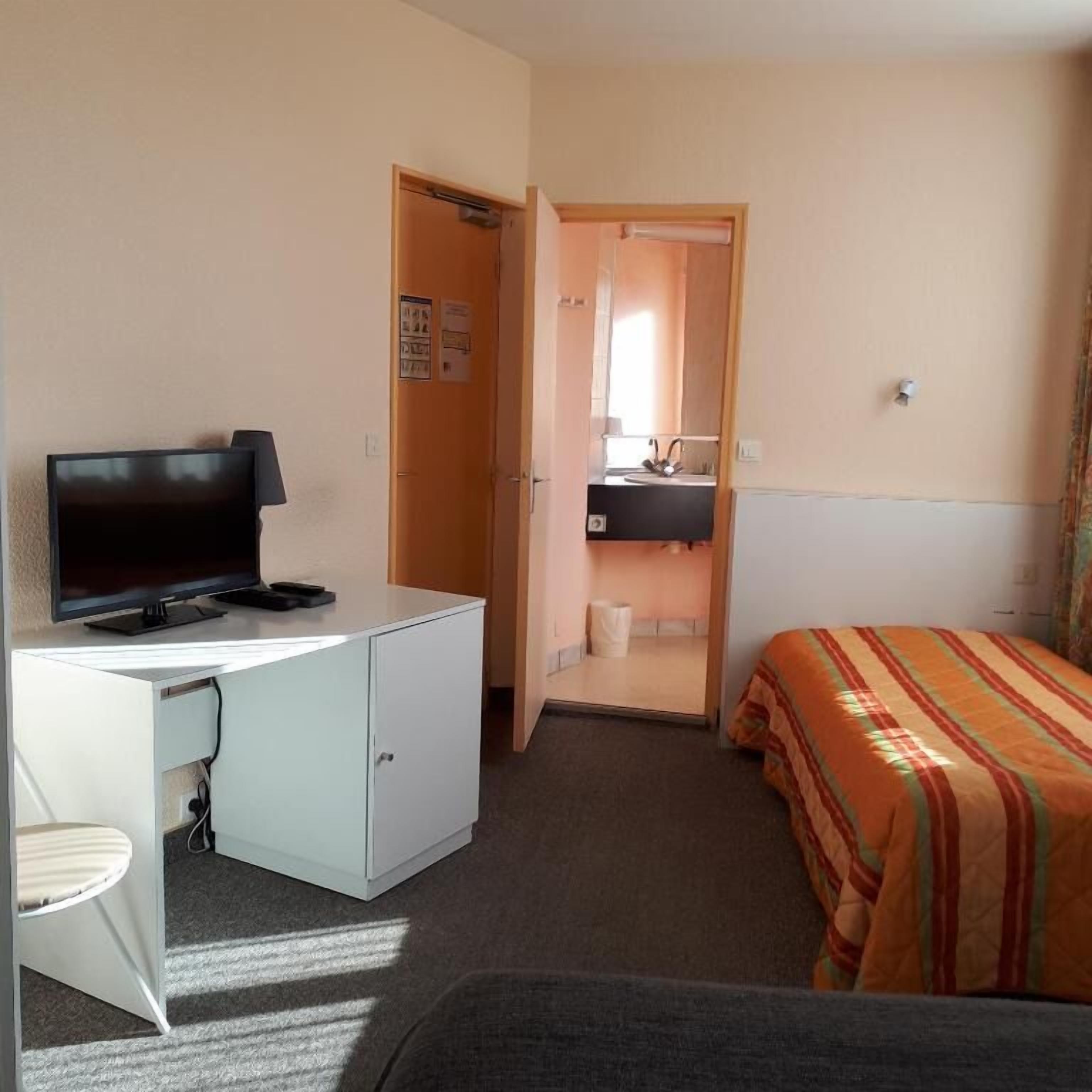 Una camera d'albergo con un letto, una scrivania con televisore, un bagno piccolo e una finestra.