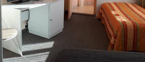 Una habitación de hotel con cama, escritorio con televisor, baño pequeño y ventana.