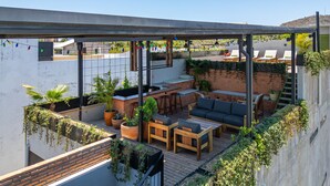 Een terras op het dak met een houten tafel en stoelen, een comfortabele zithoek en potplanten.