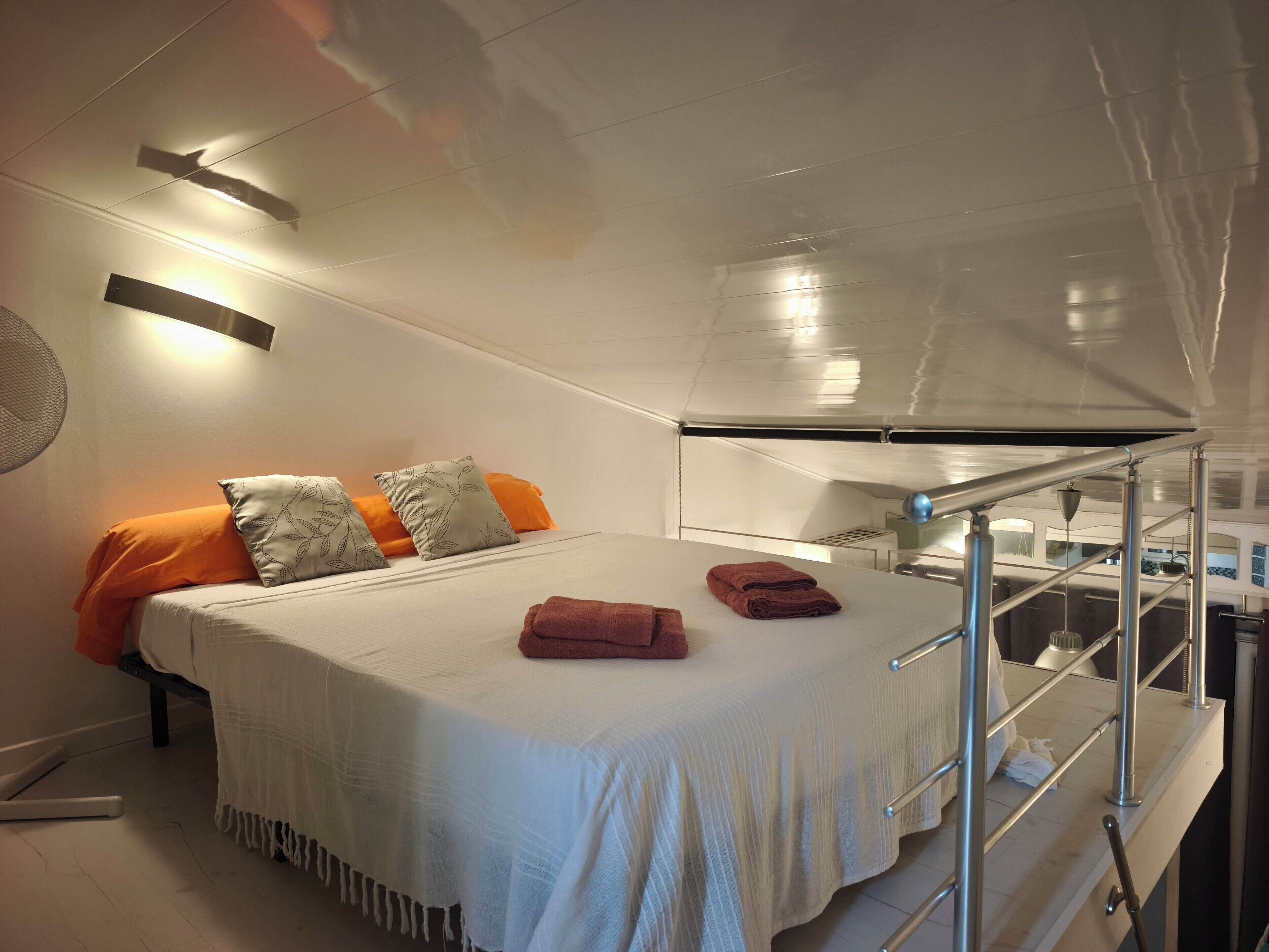 Ein modernes Hotelzimmer mit einem Bett, einem kleinen Tisch, einem Spiegel und einem Balkon mit Metallgeländern.