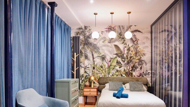 Een slaapkamer met een bed, een stoel, een nachtkastje en een muur met een tropische muurschildering.