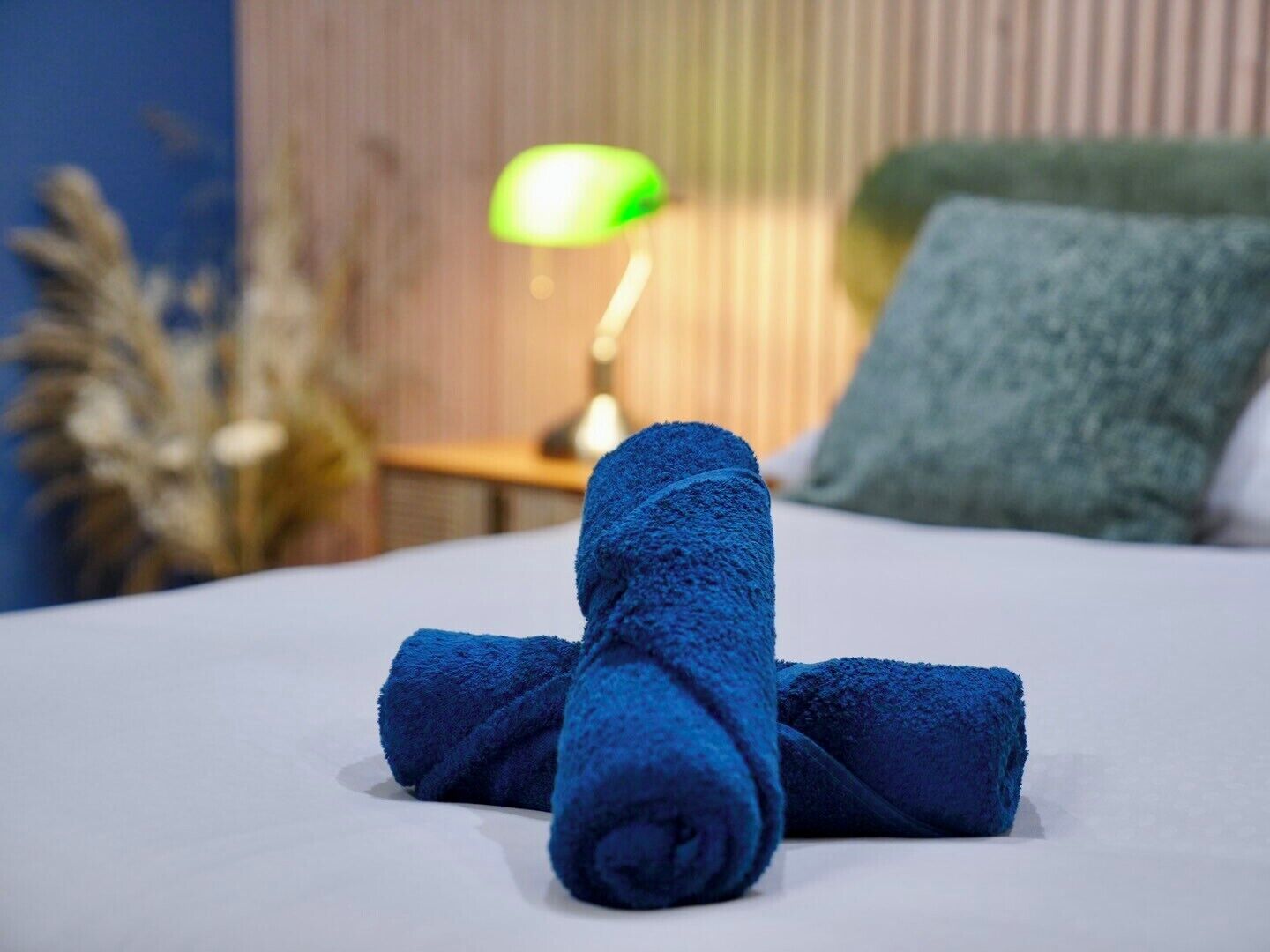 A neatly made bed with blue towels, a green lamp, and a wooden headboard.