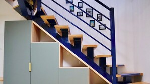 Een trap met een blauwe leuning en houten treden, leidend naar een plateau met een lichtblauwe kast en een houten ladeblok.
