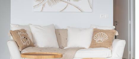 A modern living room with a white sofa, two wooden side tables, a hanging pendant light, and a wall art piece.