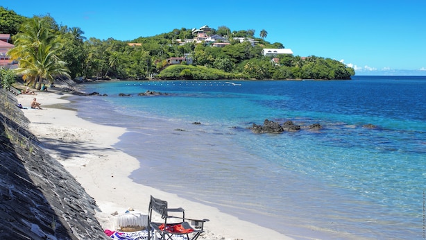 A beach with clear blue water, a chair, and a blanket on the sand. - Odyssée Bleue (Trois-Ilets)