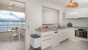 A modern kitchen with white cabinets, a dishwasher, and a view of the marina. - Odyssée Bleue (Trois-Ilets)