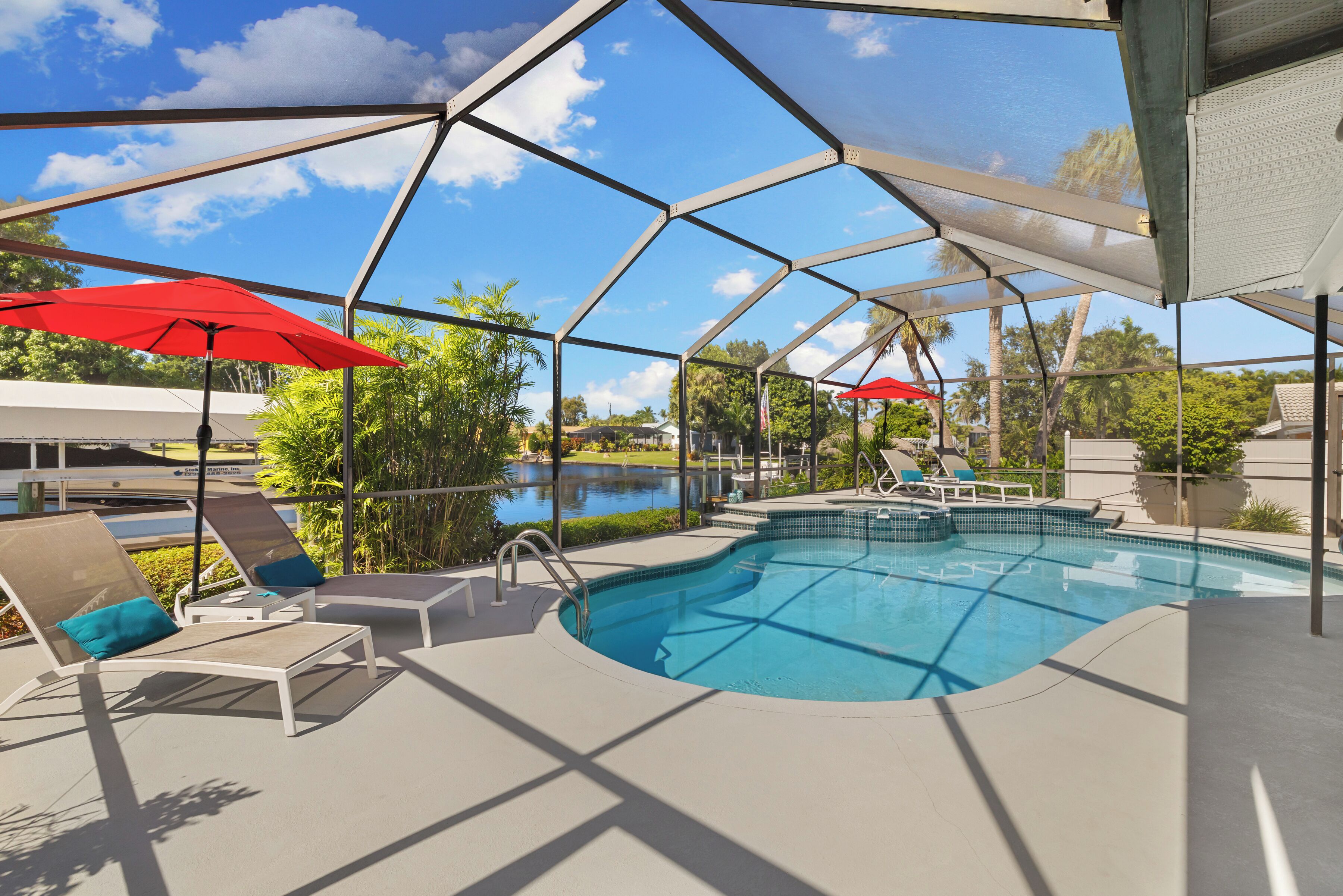 A swimming pool with a covered area, lounge chairs, and red umbrellas.