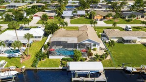 An aerial view of a residential area with a large house featuring a swimming pool, dock, and well-maintained lawn. - Seaside Villa Southern Belle - 3/2 Southeast paradise with spa and outside TV (Cape Coral)