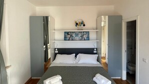 Ein Schlafzimmer mit Bett, einem Bild an der Wand und einem durchgegangenen Tür erkennbaren Badezimmer.