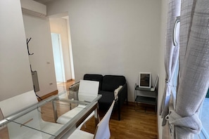 Una sala de estar moderna con una mesa de comedor de vidrio, un sofá negro y una pequeña mesita con un televisor.