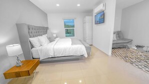Une chambre à coucher moderne avec un grand lit, une table de chevet, un téléviseur et une vue sur l’extérieur.