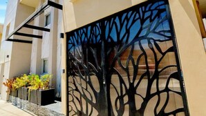 Une maison moderne à l’extérieur beige, avec un grand portail noir orné d’un motif d’arbre et une petite fenêtre au-dessus de la porte.