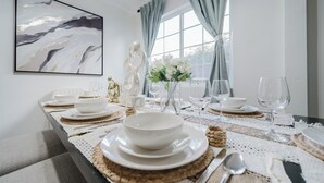 A dining table set with white plates, bowls, and cutlery, with a vase of white flowers and a decorative sculpture. - Garage, Gated Yard, near SD Gaslamp, DT, 4BR/2Bth (National City)