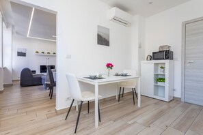 A modern kitchen with white cabinetry, a dining table with chairs, a microwave, and a small cabinet with decorative items. - Etherea Apartment with Concierge in the Heart of Catania (Catania)