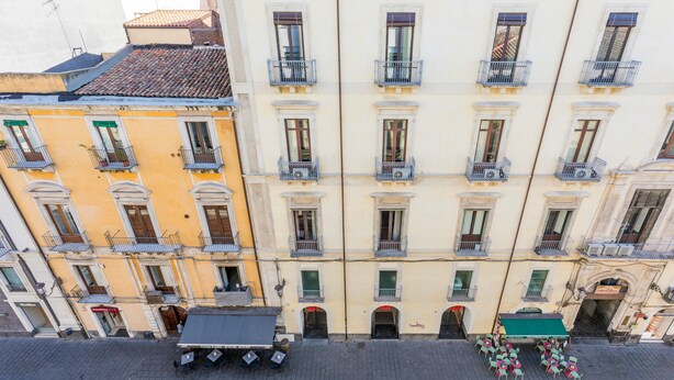Un edifici de diverses plantes amb balcons, una tenda verda i una filera de taules i cadires a l'exterior.