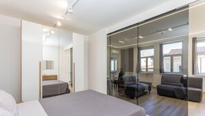 Habitació d'hotel moderna amb un llit gran, zona de seients amb sofàs, un separador de vidre i vista a l'exterior.
