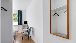 Een slaapkamer met een bed, een bureau, een stoel, een spiegel en een raam met gordijnen.