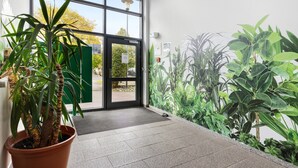 Een hotelentree met een grote glazen deur, plantenbakken en een groen muurdecoratie.