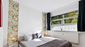 Een slaapkamer met een bed, nachtkastjes, een raam met gordijnen en een radiator.