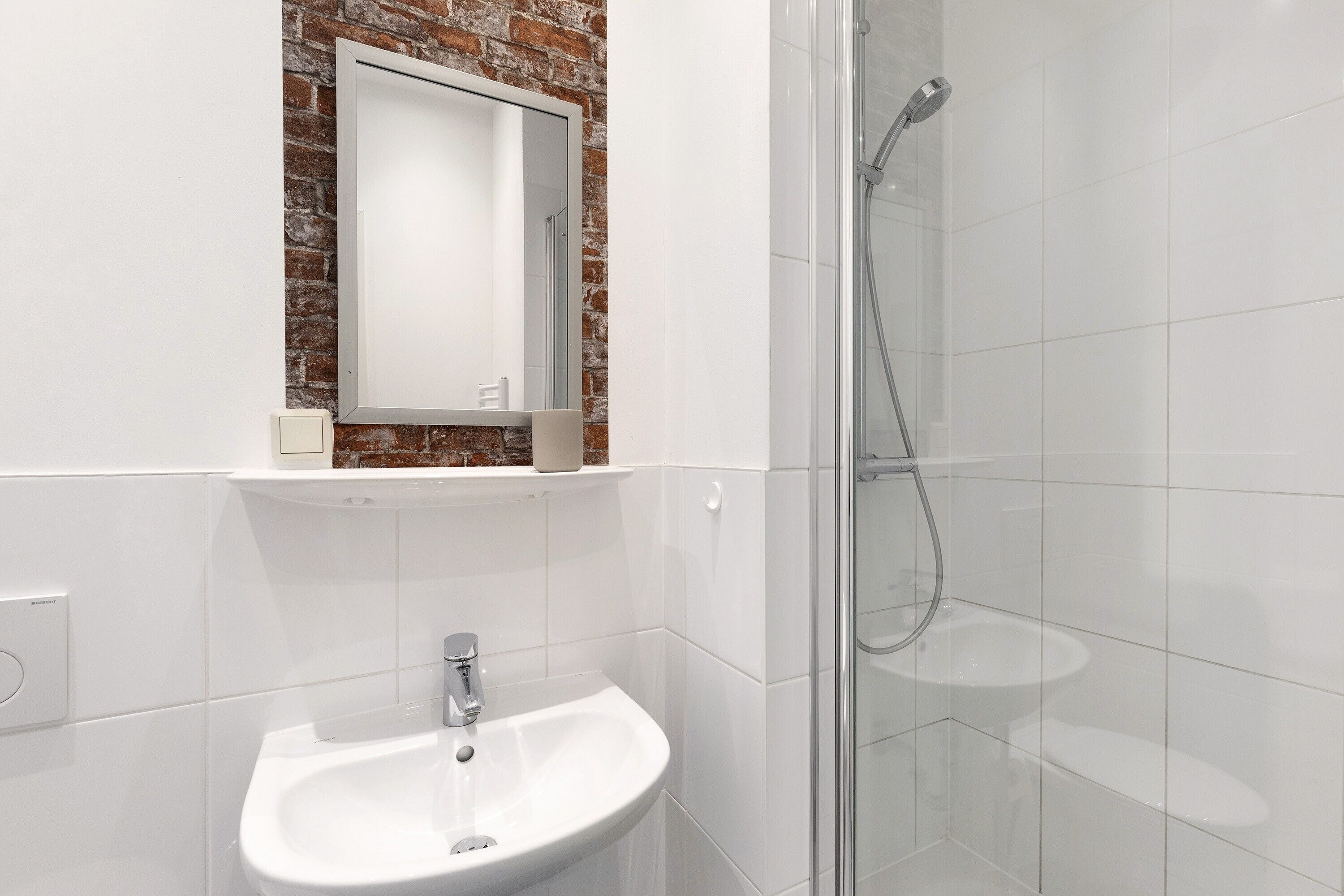 Ein Badezimmer mit einem weißen Waschbecken, einem Spiegel darüber und einer Glasdusche.