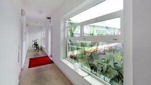 Een gang met een fiets, een rode mat en een raam met planten.