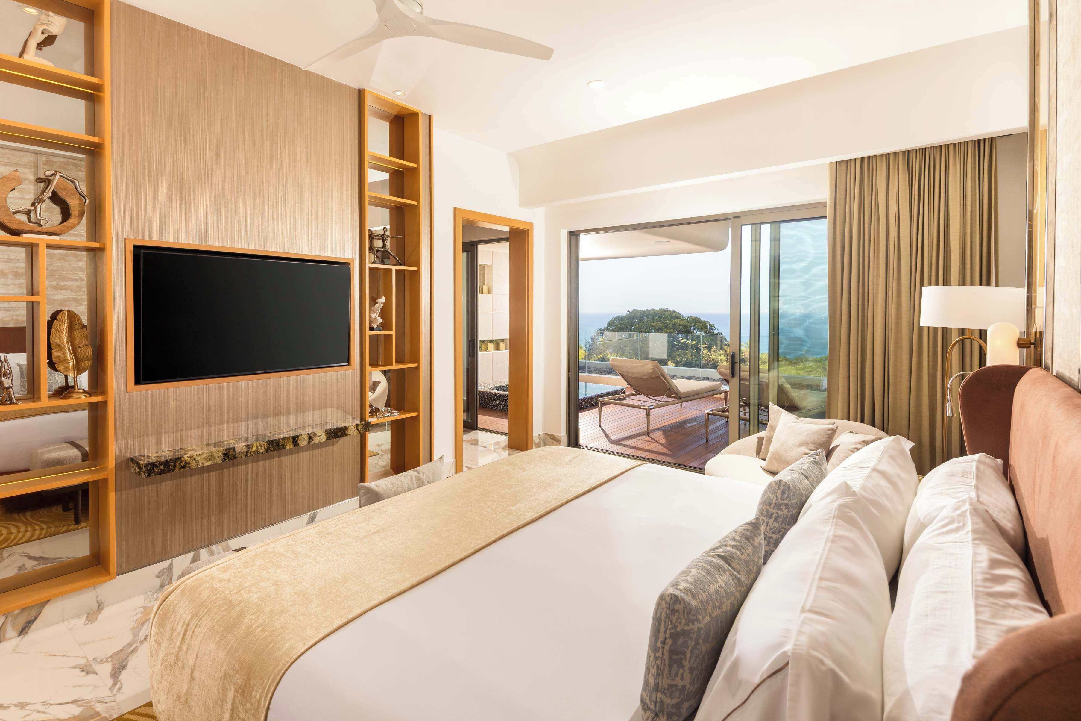 Une chambre d’hôtel avec un grand lit, une télévision, un balcon avec vue et une étagère en bois agrémentée d’objets décoratifs.