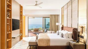Quarto de hotel com cama, televisão, varanda com cadeira e vista para o mar.