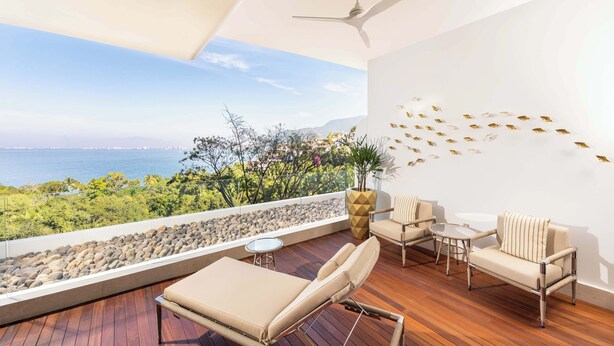 Un balcón con vista al mar, ventilador de techo y zona de estar con mesa y sillas.