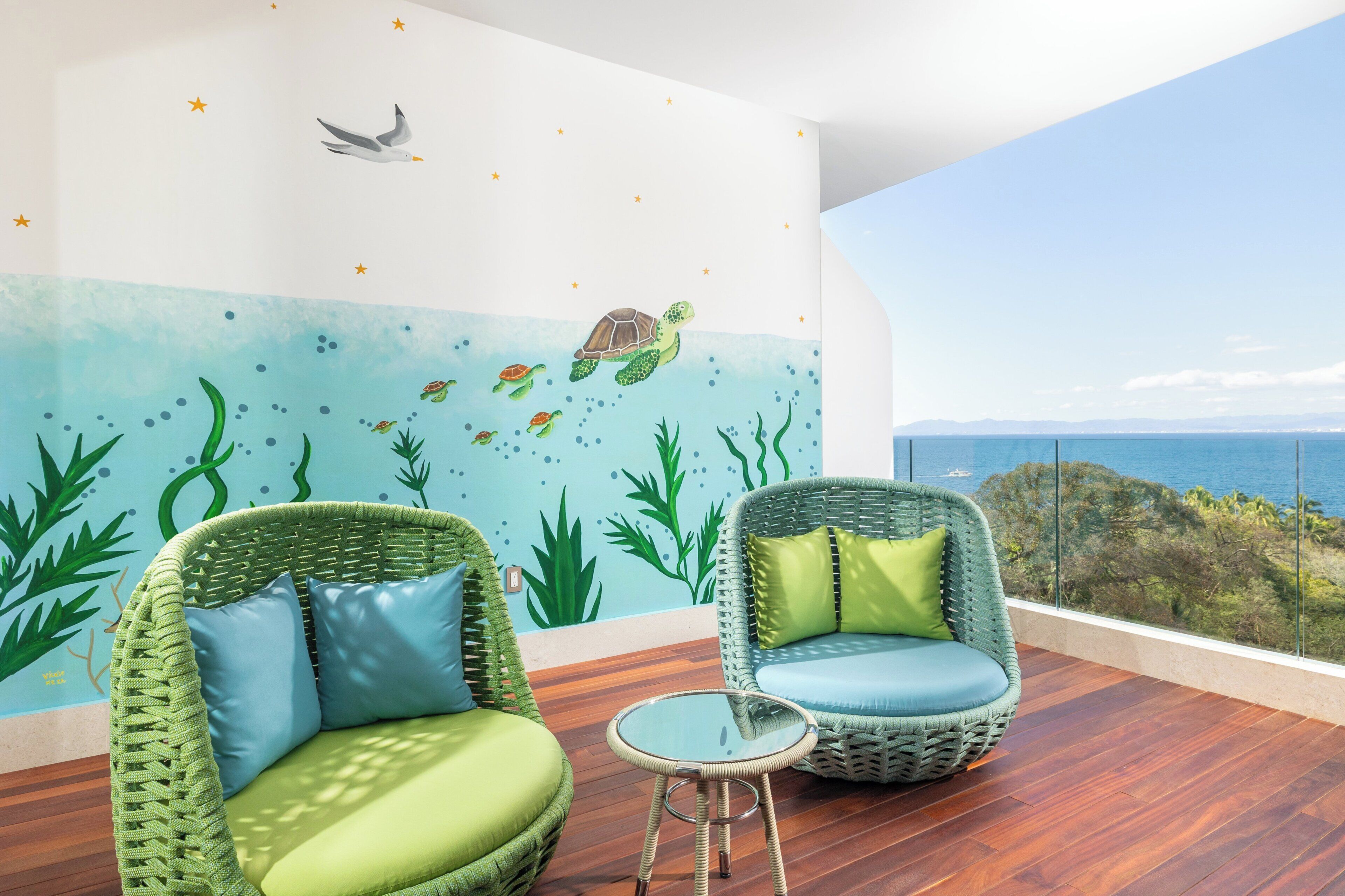 A balcony with wicker chairs, a small table, and a mural of sea life.
