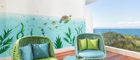 A balcony with wicker chairs, a small table, and a mural of sea life.