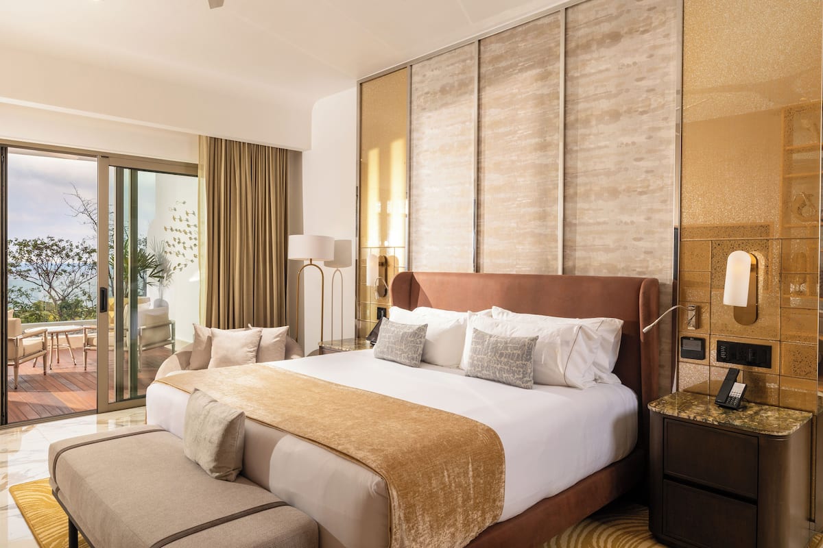 A modern hotel room with a large bed, a bedside table with a phone, and a sliding glass door leading to an outdoor area.